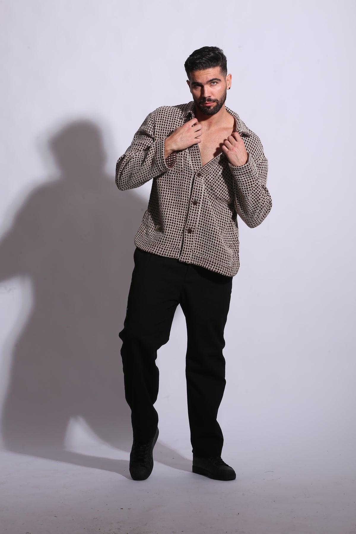 Man wearing a patterned coat and black pants against a white background