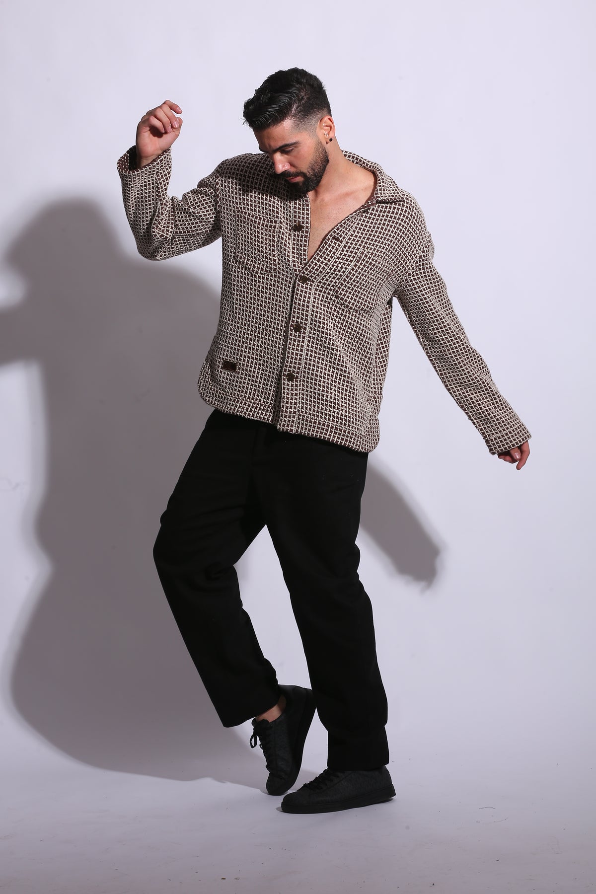 Man wearing a patterned jacket and black pants on a white background