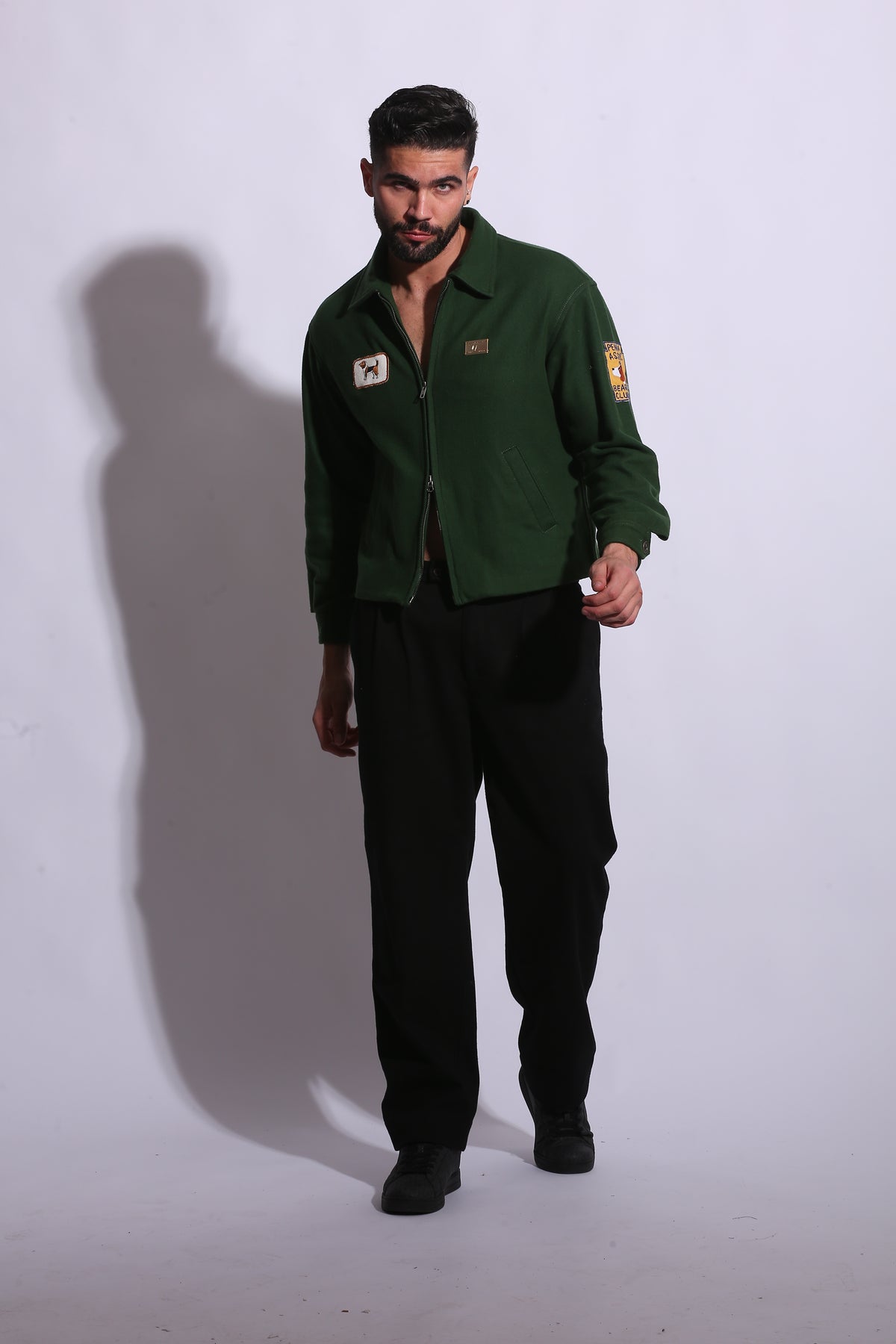 Person wearing a green jacket and dark pants on a white background