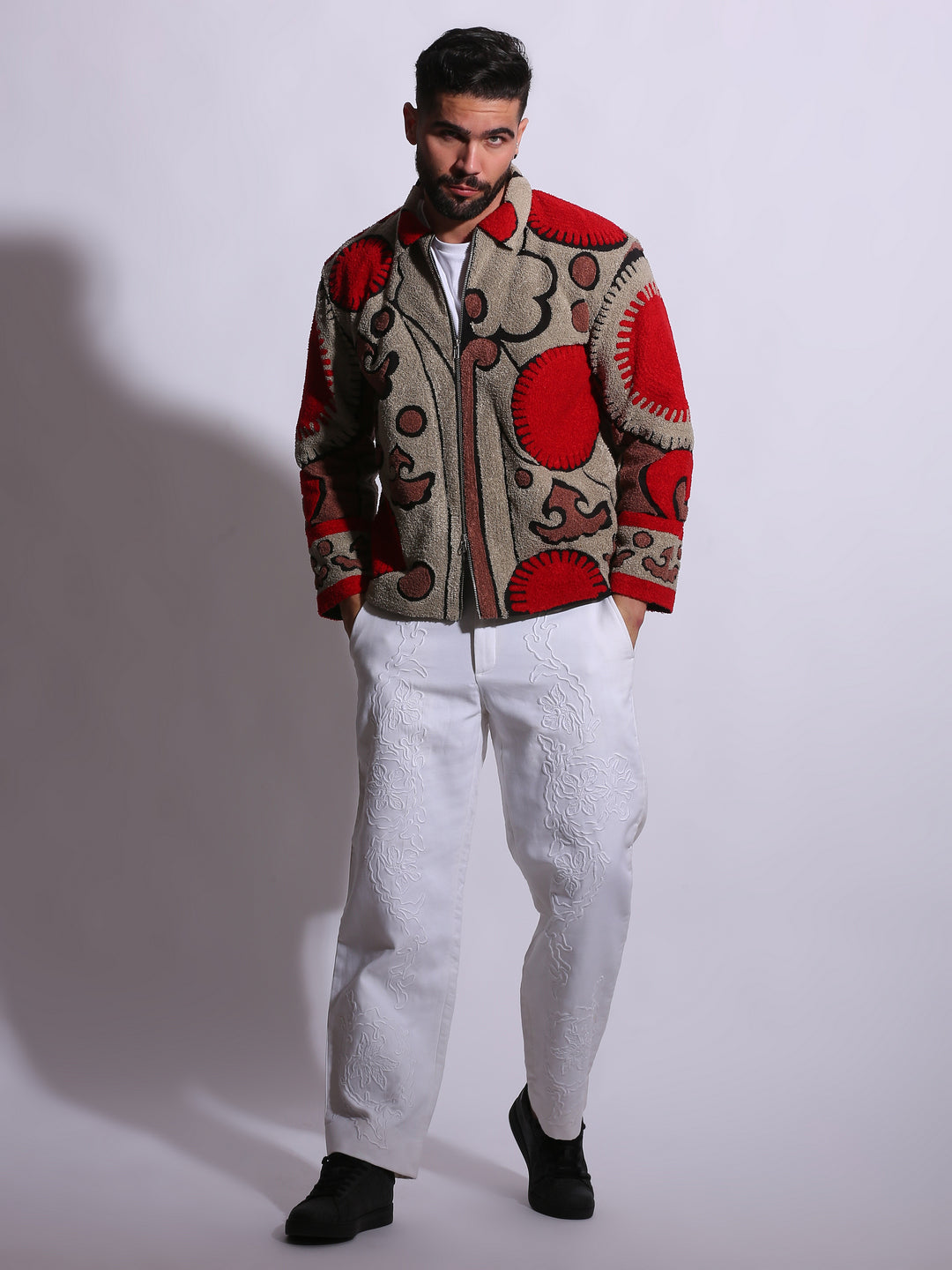Man wearing a patterned jacket and white pants on a plain background