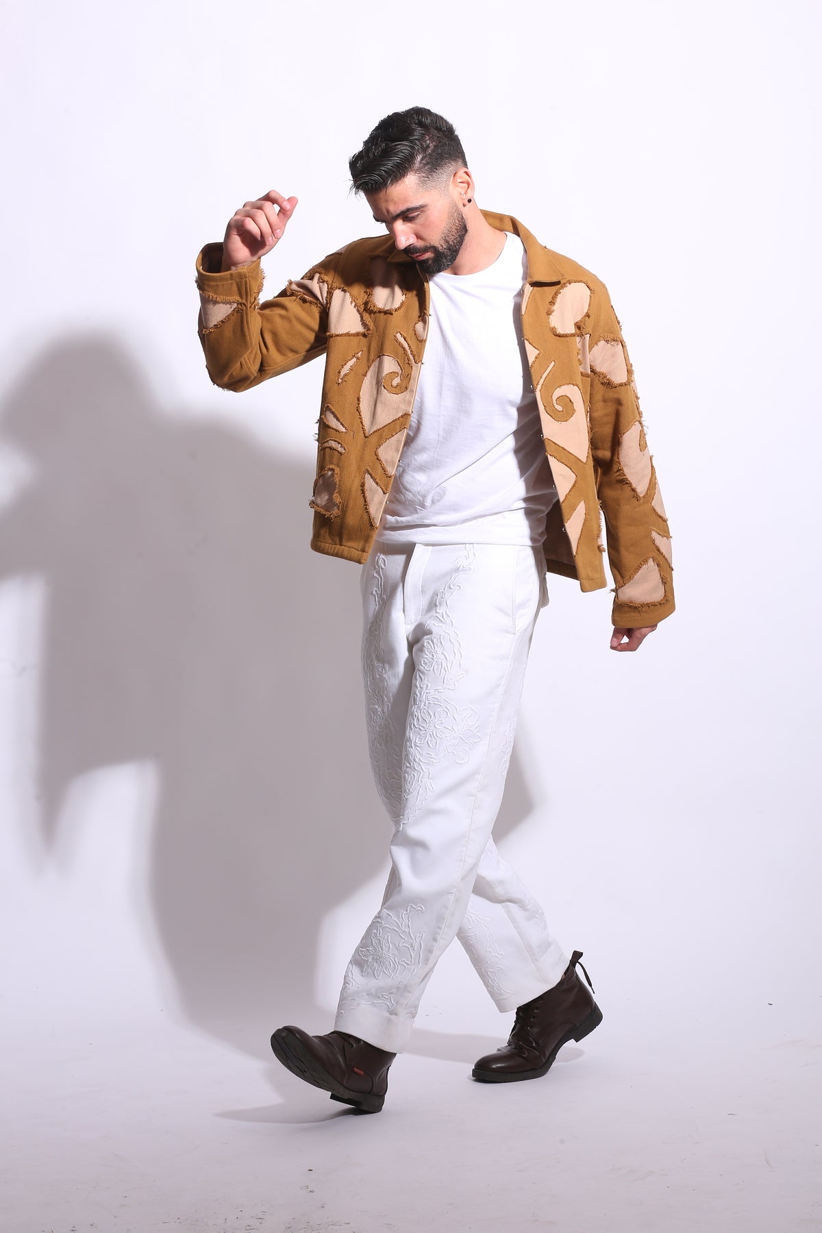 Man wearing a patterned shirt and white pants on a white background