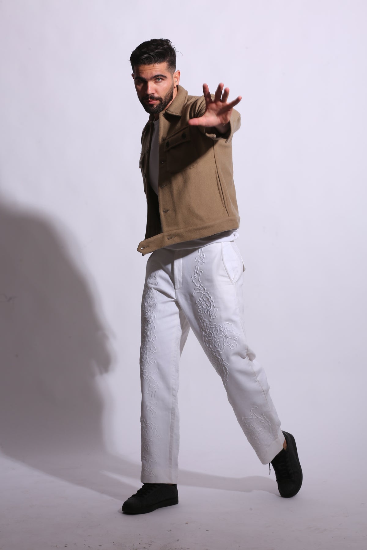 Person wearing a beige coat and white pants on a white background
