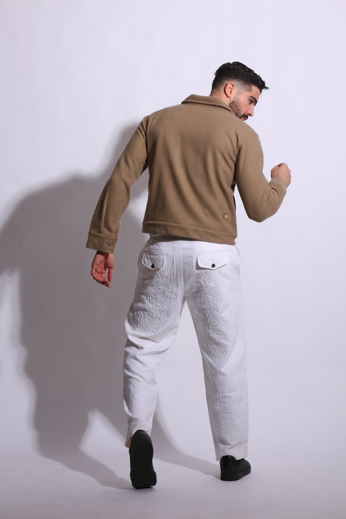 Man wearing a brown coat and white pants on a white background
