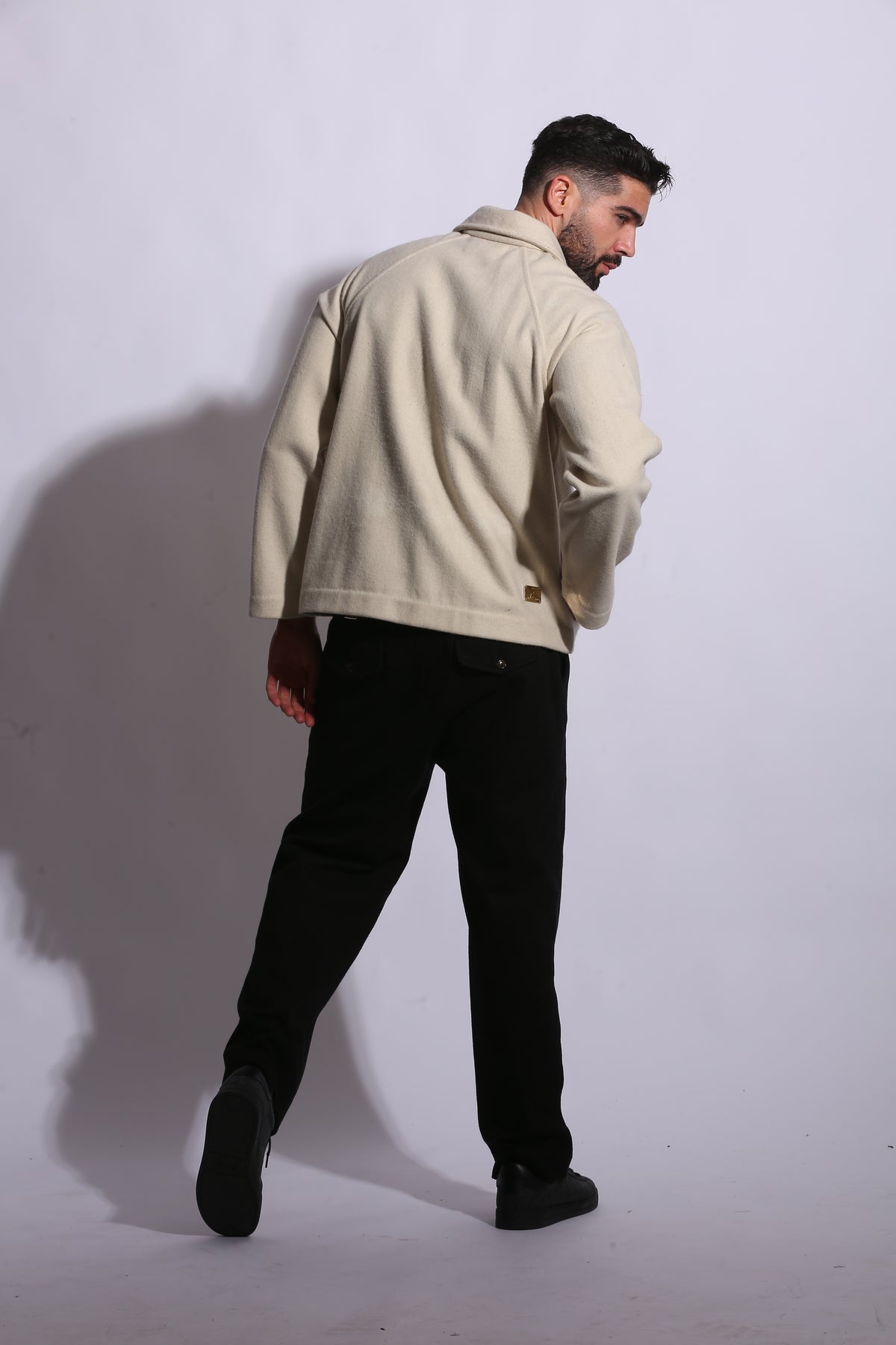 Person wearing a beige coat and black pants on a white background