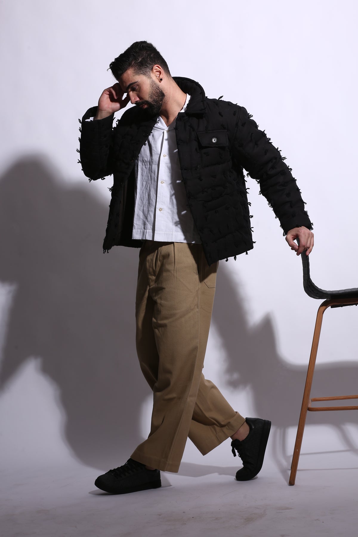 Man in a black coat and beige pants standing on a white background