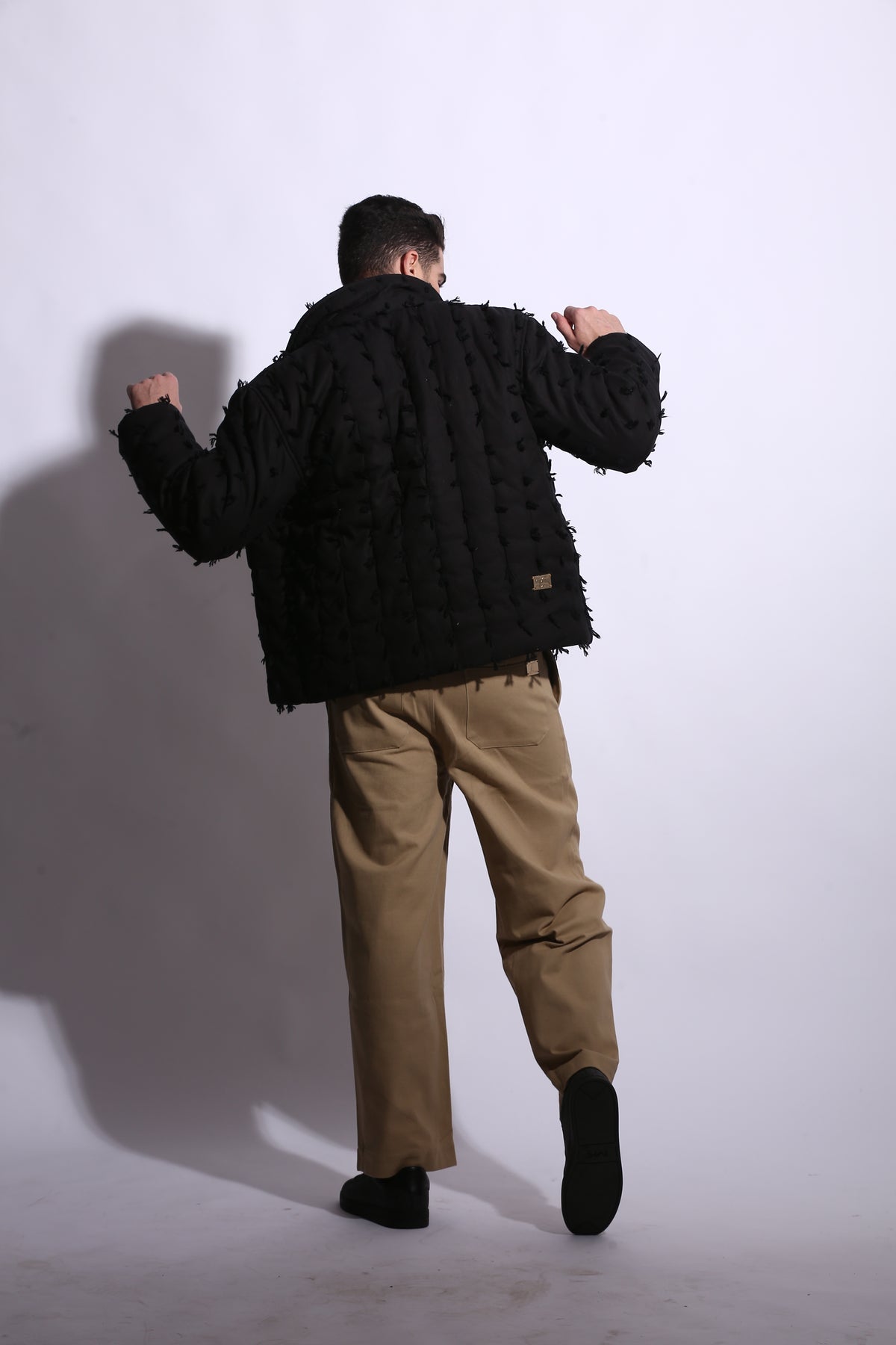 Person wearing a black textured jacket and beige pants on a white background