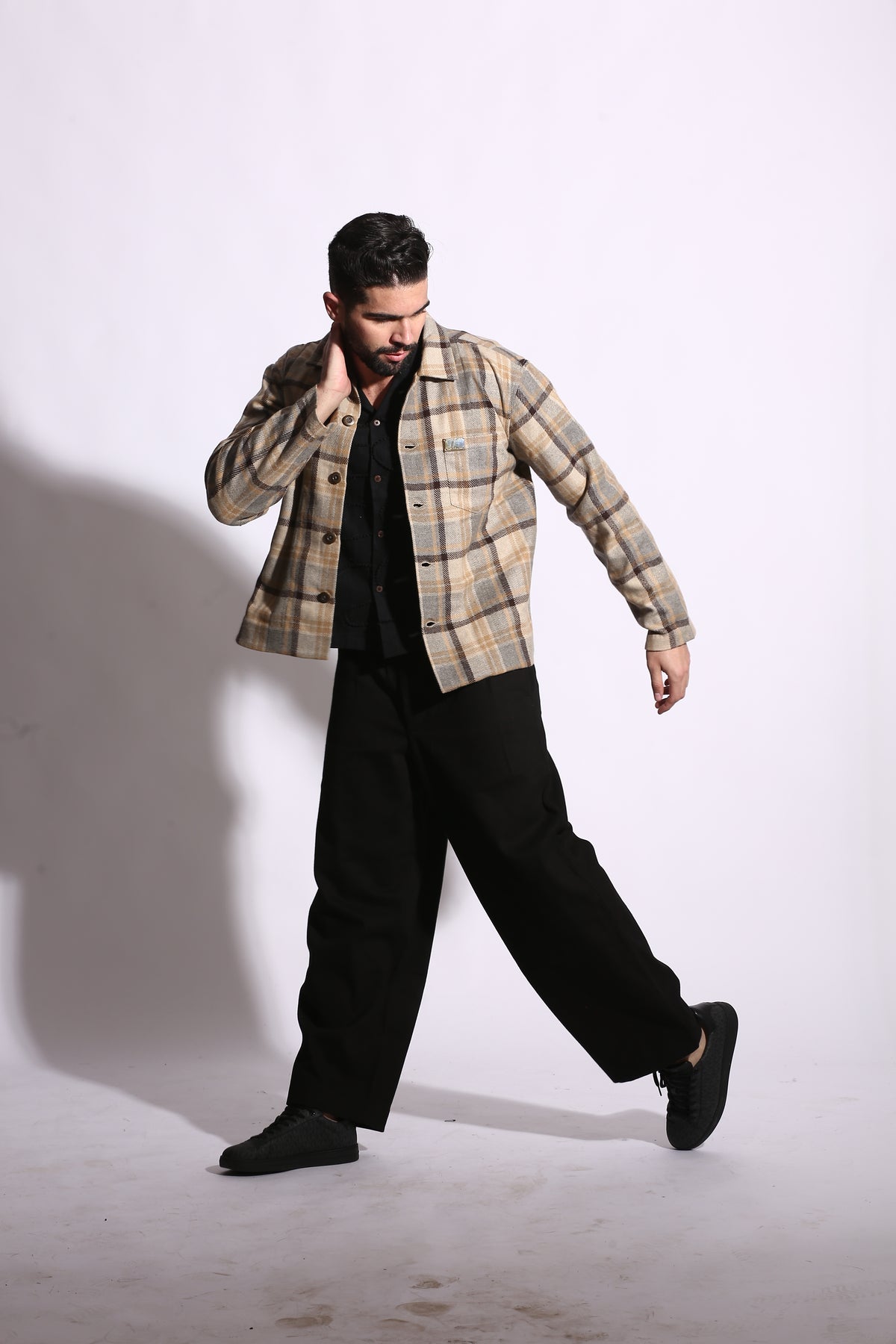 Person wearing a plaid shirt and black pants on a white background