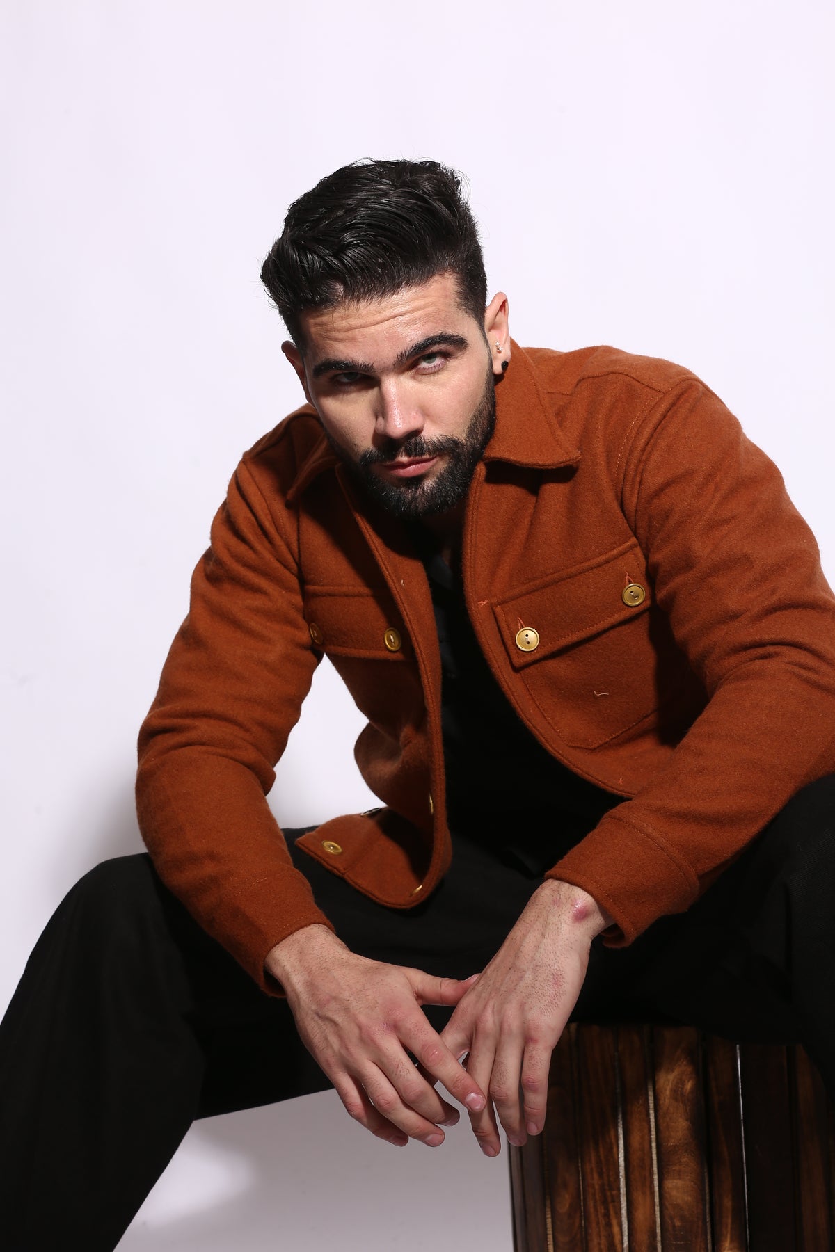 Man wearing a brown coat sitting on a wooden bench against a white background