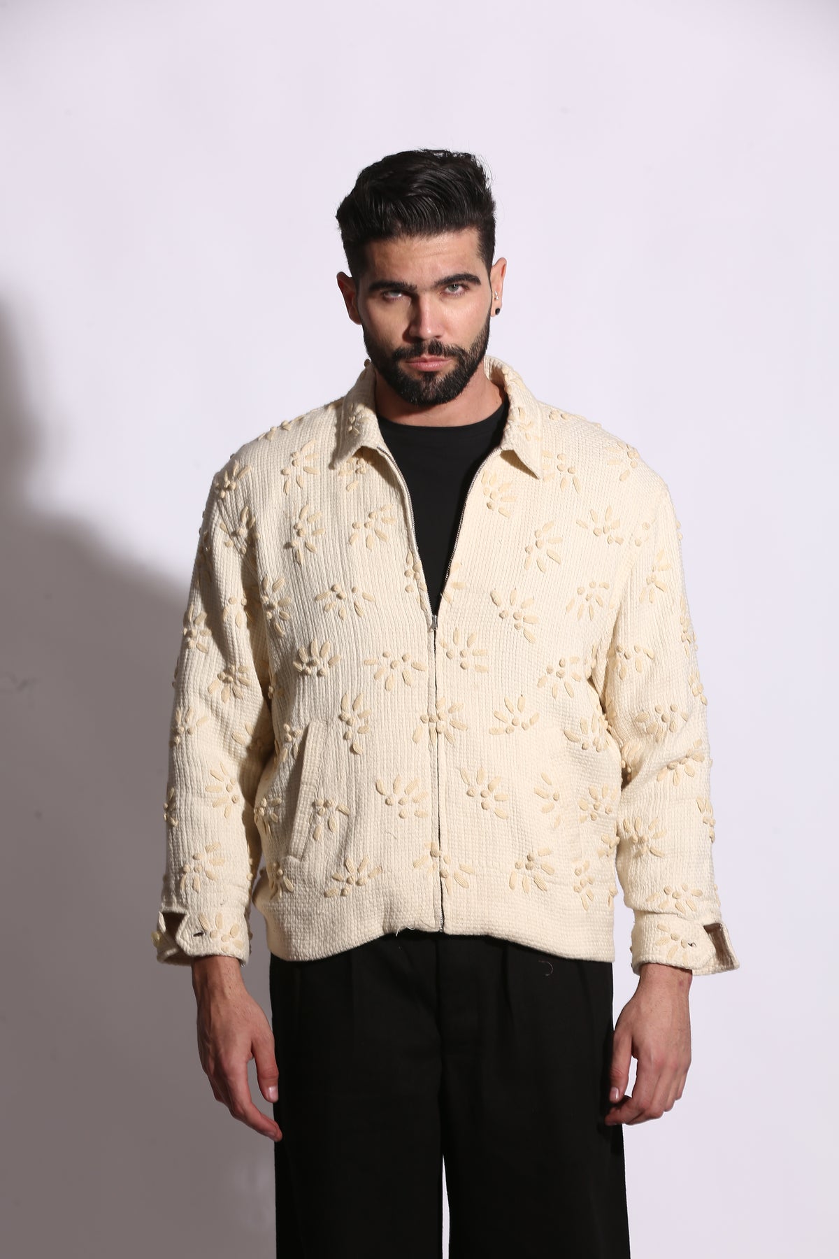 Man wearing a cream-colored embroidered jacket on a plain background