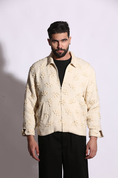 Man wearing a cream-colored embroidered jacket on a plain background