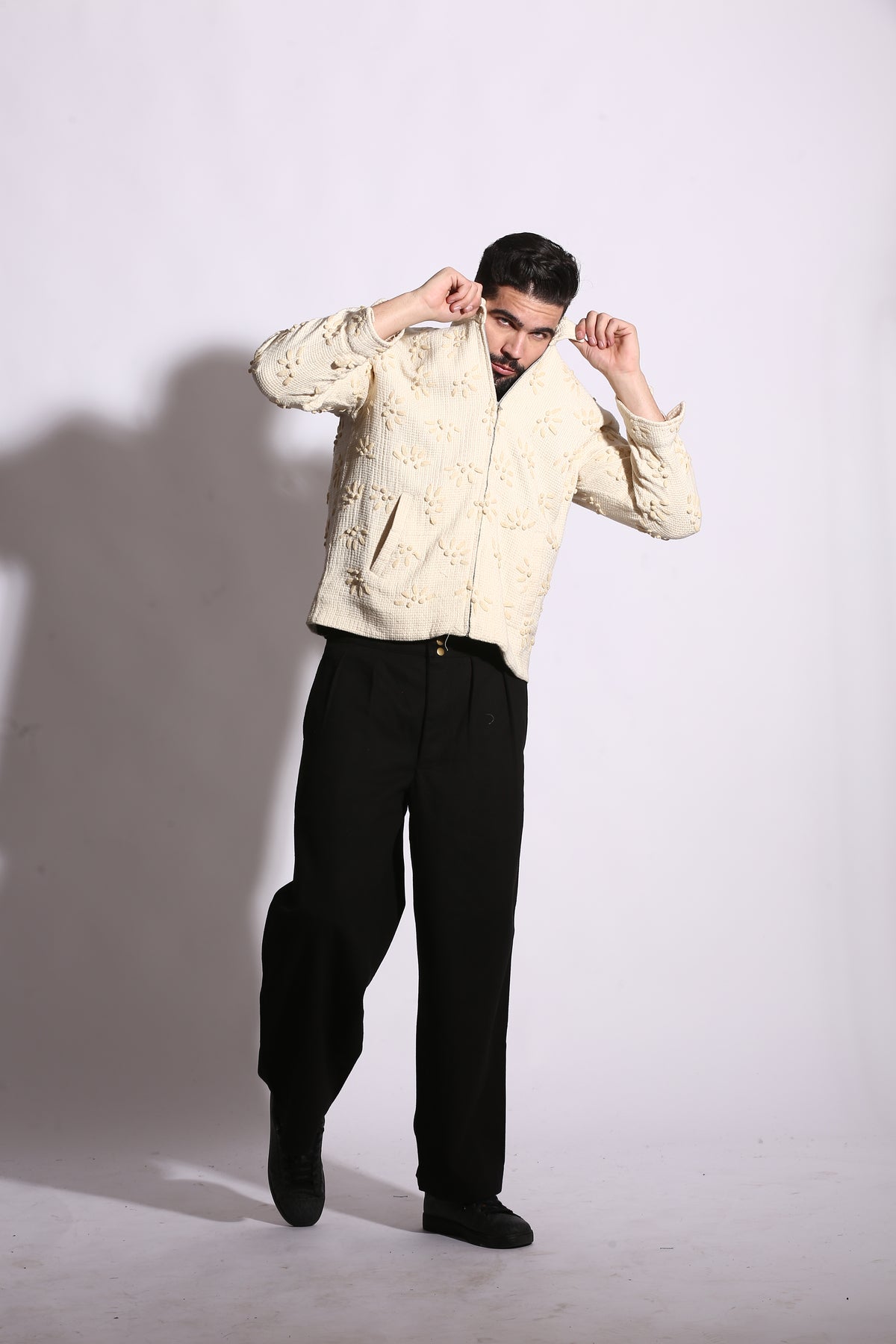 Person wearing a beige jacket and black pants on a white background