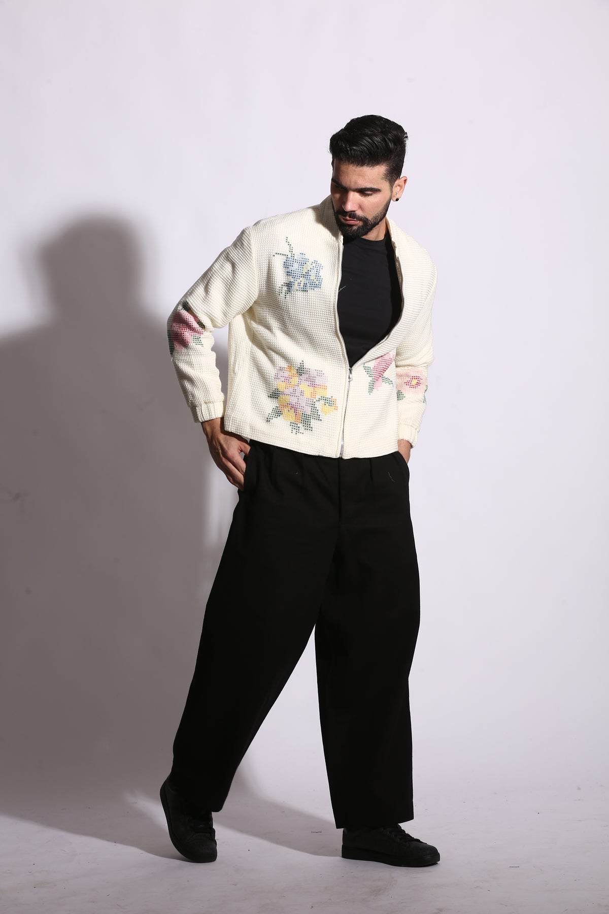 Person wearing a white embroidered jacket and black pants on a white background
