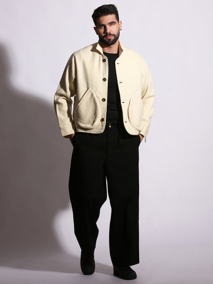Man wearing a beige jacket and black pants against a plain background