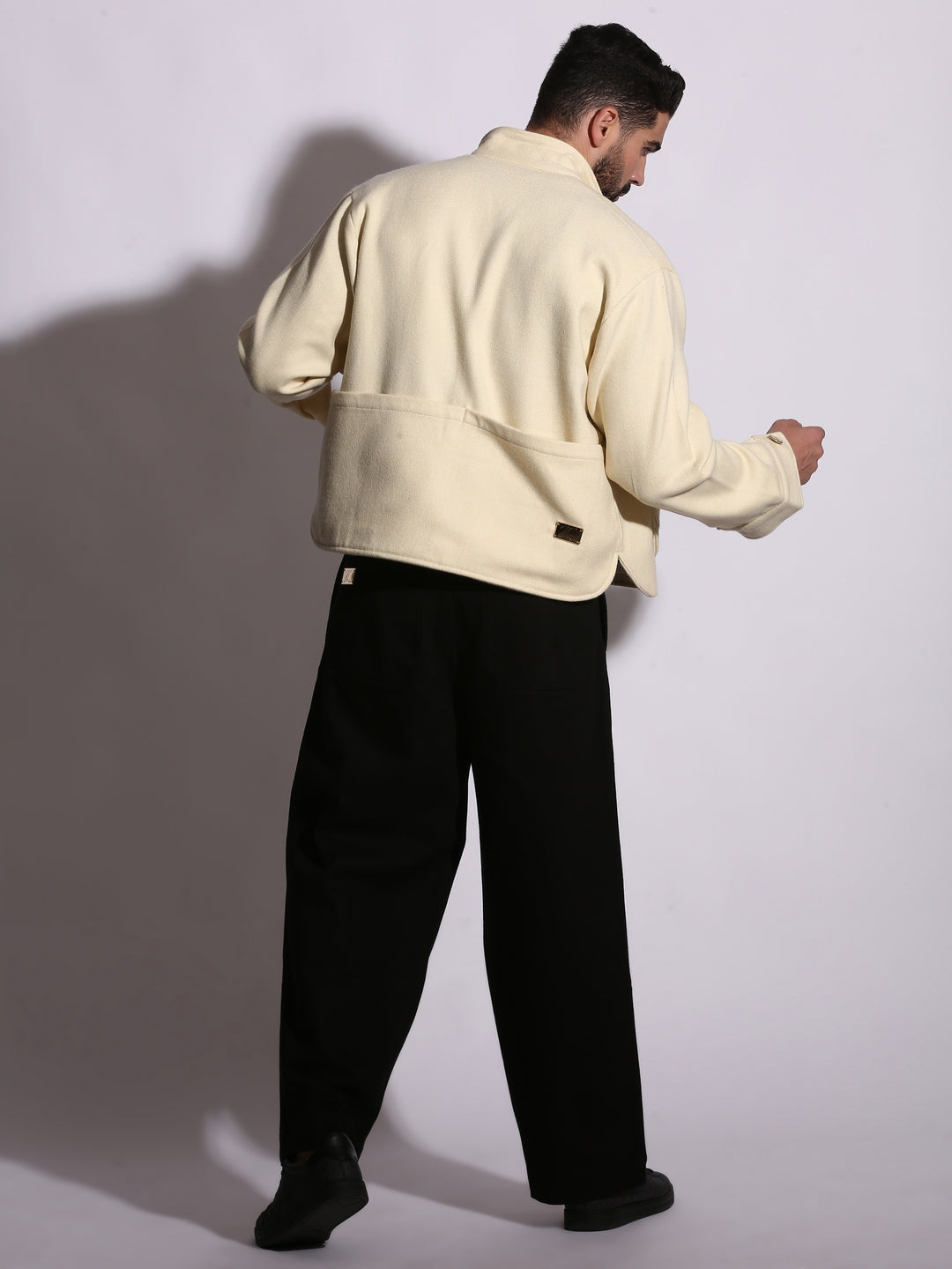 Man wearing a cream jacket and black pants against a white background