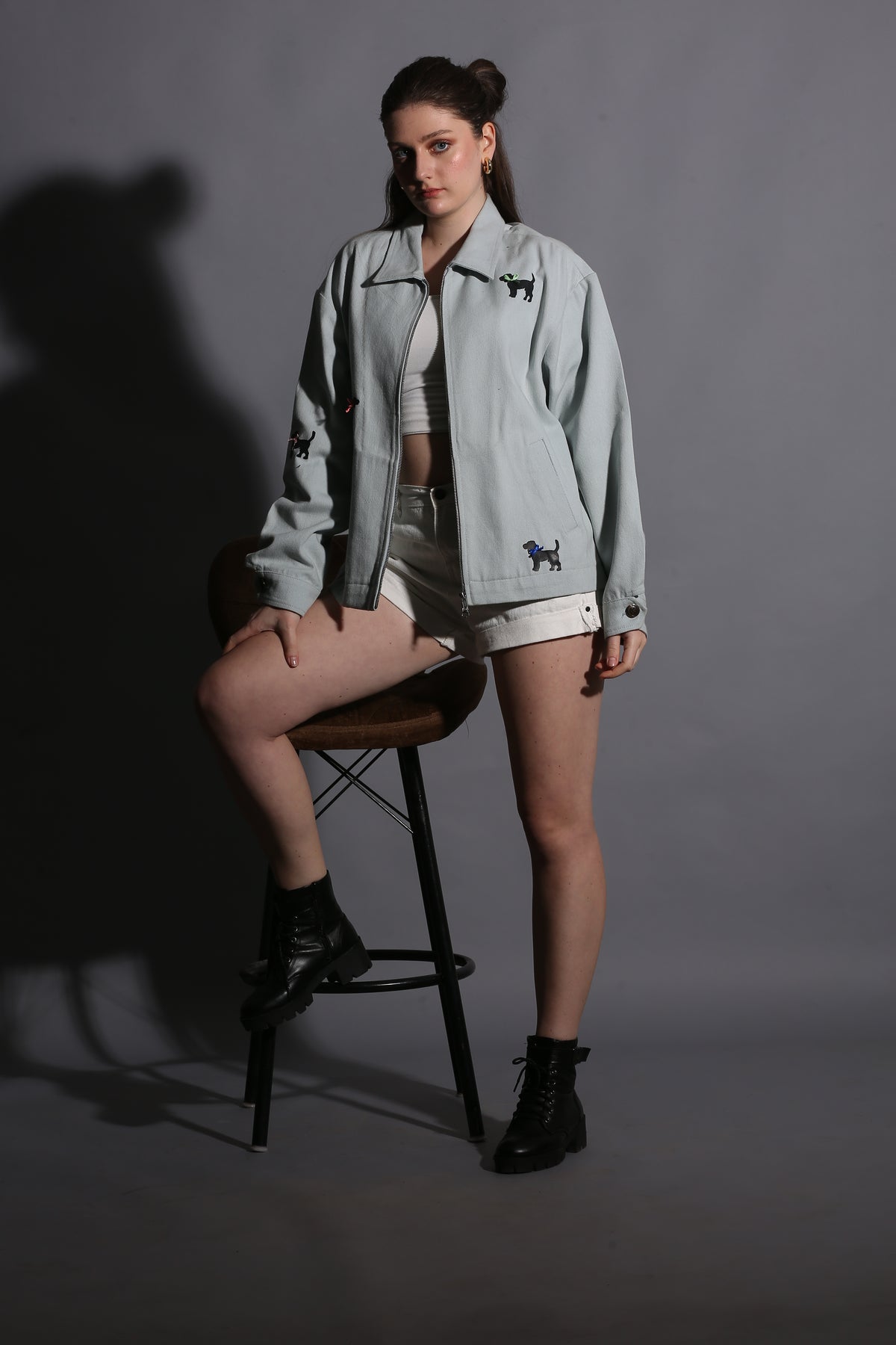Person wearing a light gray jacket with a dark logo on a gray background