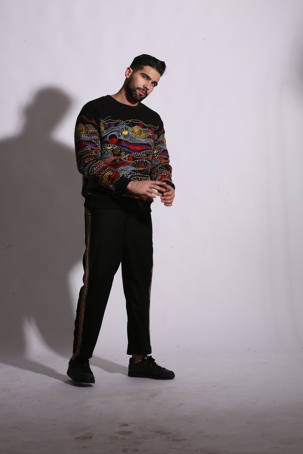 Person wearing a colorful sweater and black pants on a white background