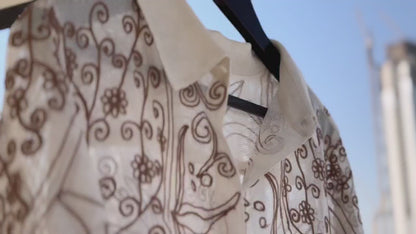 Set in a soft beige tone, the shirt is defined by its intricate chain stitch embroidery, creating a rich, textured surface that adds depth without overpowering the design.